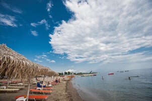 Una playa con sombrillas de paja, tumbonas y agua tranquila.