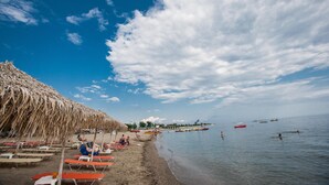 Een strand met rieten parasols, ligbedden en rustig water.