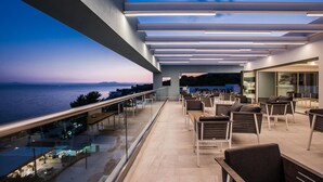 Een dakterras met buitenmeubilair, een glazen balustrade en uitzicht op zee.