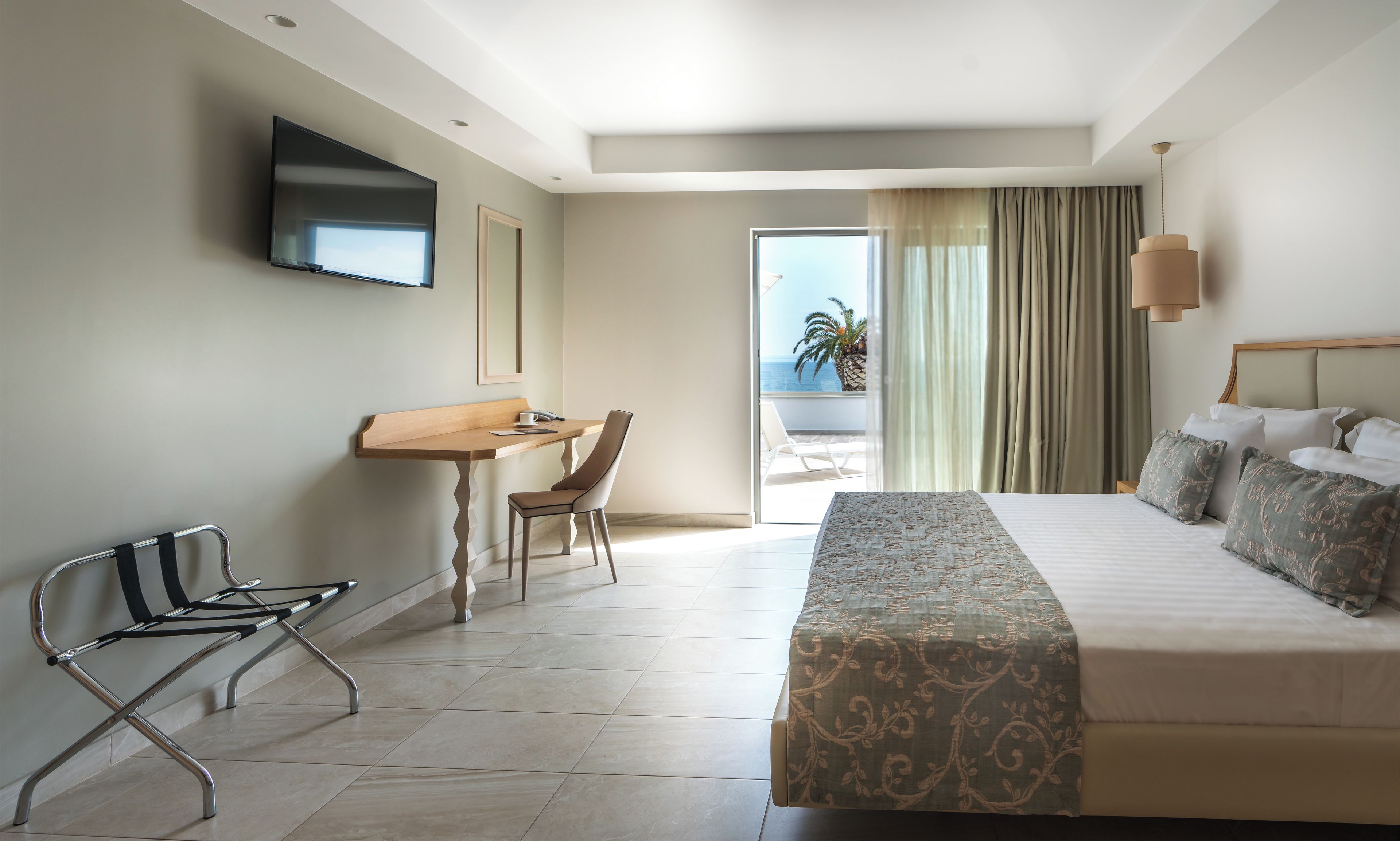 Habitación de hotel con cama, escritorio, silla, televisión y vista al océano.