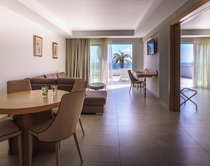A modern hotel room with a dining area, a sofa, a small table, and a TV mounted on the wall.
