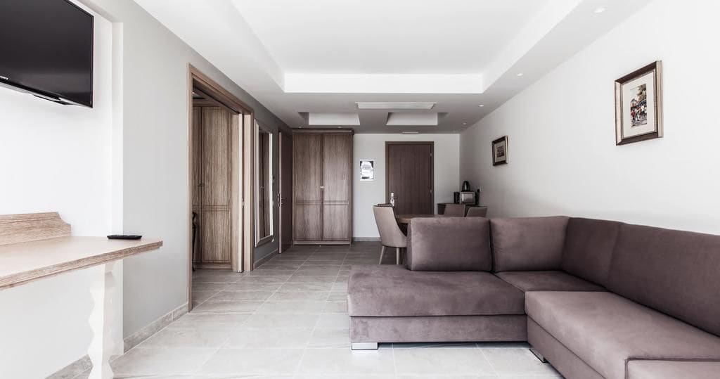 A modern living room with a sectional sofa, a flat-screen TV mounted on the wall, and a dining area with a table and chairs.