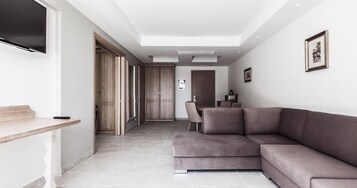 Una sala moderna con un sofá modular, un televisor de pantalla plana montado en la pared y un comedor con mesa y sillas.