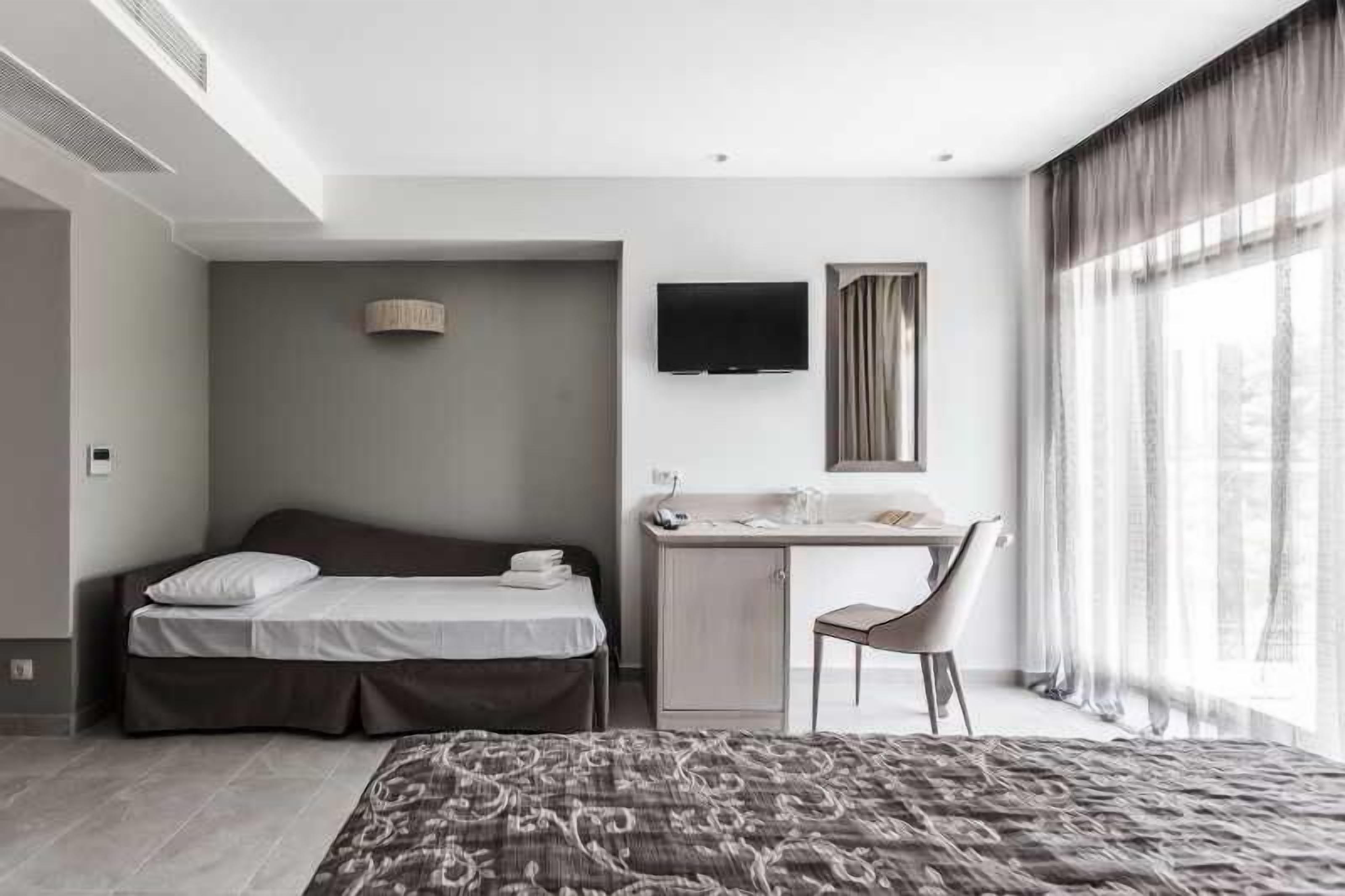 Una camera d'albergo con un letto, una scrivania, una sedia, televisione e ampie finestre.
