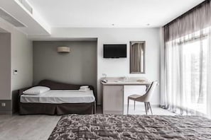 A hotel room with a bed, desk, chair, TV, and large windows. - Elinotel Sermilia (Polygyros)