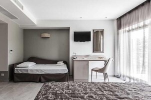 A hotel room with a bed, desk, chair, TV, and large windows.