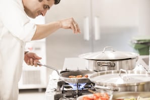 A person cooking with a pan on a stove, pots, and a kitchen counter.