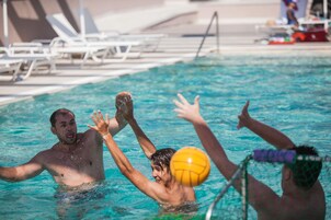 Una piscina con gente jugando, sillas de descanso y zona de borde de piscina.