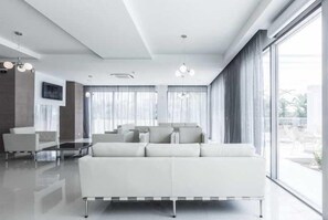 A modern living room with a white sofa, a glass coffee table, and large windows with curtains.