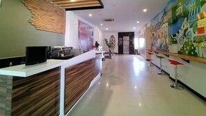 A modern reception area with a wooden reception desk, a flat-screen TV, and a 'OPENING' sign. - Front One Green Boutique Hotel Abepura (Jayapura)