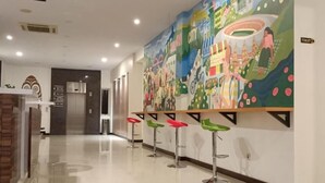 A hotel lobby with a colorful mural, a reception desk, and a row of colorful bar stools. - Front One Green Boutique Hotel Abepura (Jayapura)