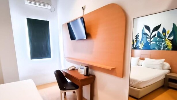 A hotel room with a bed, a desk, a chair, a TV mounted on the wall, and a large mirror reflecting the bed and a painting. - Front One Green Boutique Hotel Abepura (Jayapura)