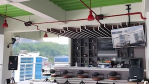Un espace bar moderne, doté d’un téléviseur, d’étagères remplies de bouteilles et offrant une vue sur les bâtiments.