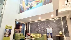 Un hall d’entrée spacieux avec un plafond haut, une grande fresque murale et un coin salon comprenant un canapé et des fauteuils.