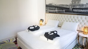 A double bed with white linens, a tufted headboard, and two black bags on the bed. There is a framed black and white cityscape painting above the bed. - A Hotels (Brondby)
