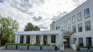 A modern building with a covered entrance, large windows, and a statue in front. - A Hotels (Brondby)