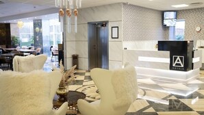 A hotel reception area with a modern design, featuring a reception desk, plush white chairs, a decorative vase, and a patterned floor. - A Hotels (Brondby)
