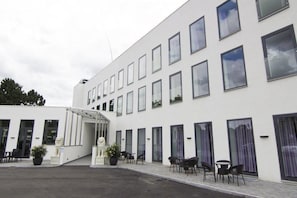 A modern building with a white facade, multiple windows, and outdoor seating area with chairs and tables. - A Hotels (Brondby)