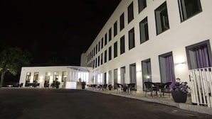 Un bâtiment moderne doté de nombreuses fenêtres et d’un espace extérieur aménagé avec des sièges, protégé par un auvent.