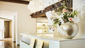 A reception desk with a vase of flowers, a chandelier, and a framed picture. - Hotel Uzwil - Ihr Businesshotel (Uzwil)