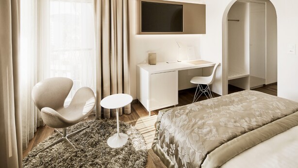 A hotel room with a bed, a desk, a chair, a TV, and a window with curtains. - Hotel Uzwil - Ihr Businesshotel (Uzwil)