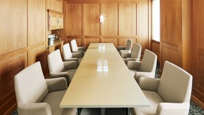 A conference room with a long table, multiple chairs, wooden paneling, and a small window. - Hotel Uzwil - Ihr Businesshotel (Uzwil)