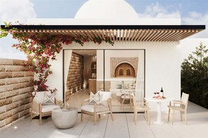 A modern outdoor seating area with wicker chairs and a round table, a white wall with a decorative arch, and a brick wall with climbing plants. - Fort Arabesque The Villas (Makadi Bay)