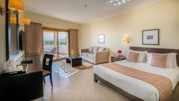 A hotel room with a bed, a desk, a chair, a sofa, a balcony with a view, and a dining area. - Fort Arabesque The Villas (Makadi Bay)
