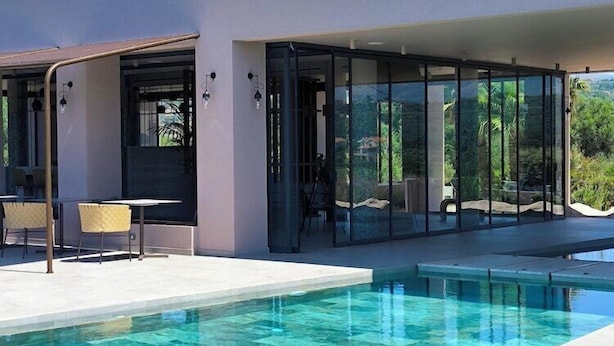 A modern outdoor pool area with a glass-enclosed patio, seating, and a clear view of the surrounding landscape. - Tetra Resort and Spa (Kefalonia)