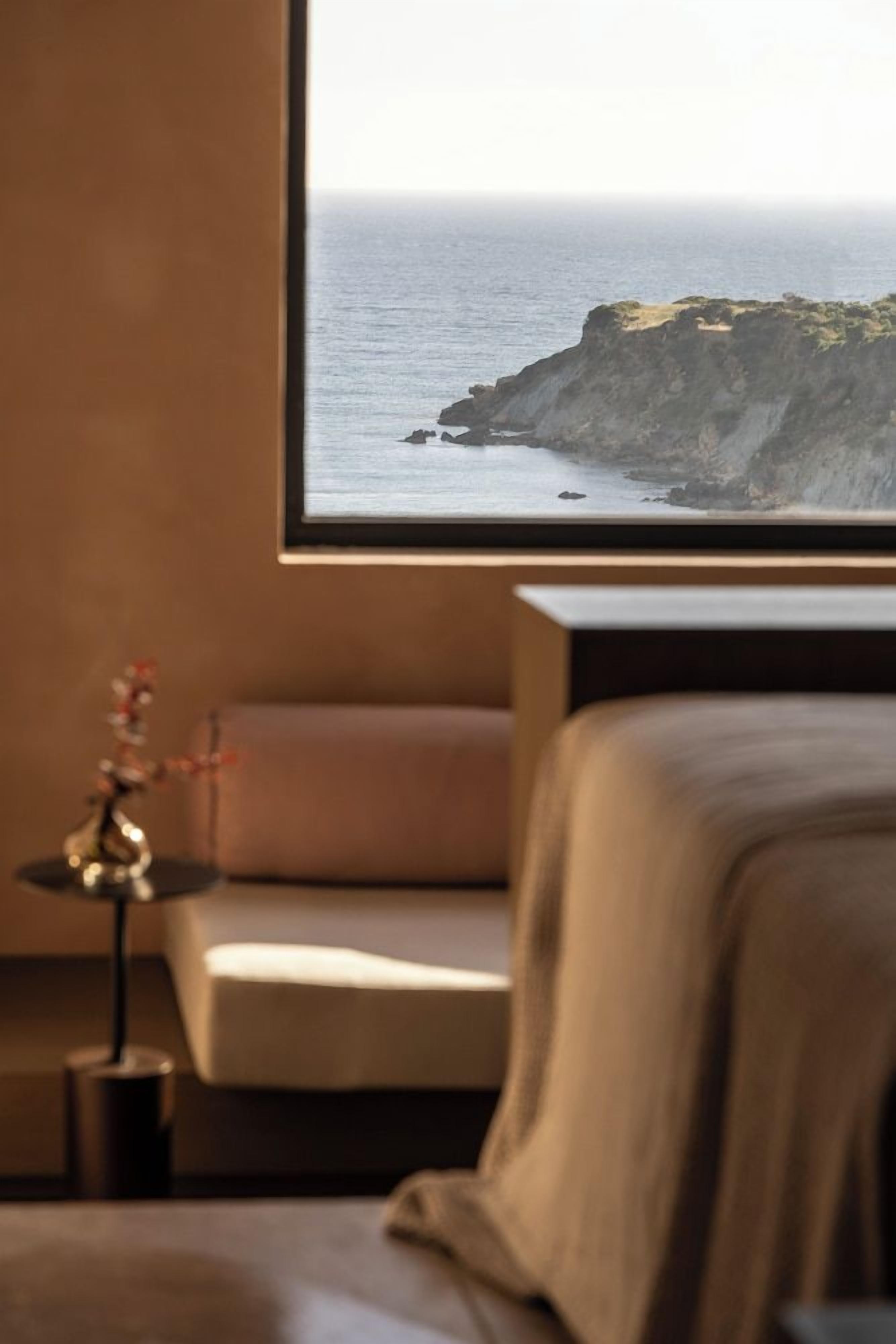 A room with a bed, a nightstand, and a framed picture of a coastal landscape.