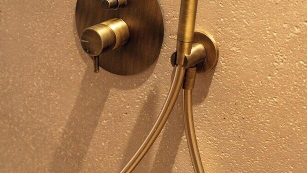 A brass shower control with two handles and a single-handle showerhead mounted on a textured wall. - Tetra Resort and Spa (Kefalonia)