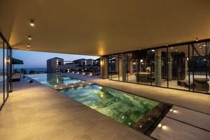 Zona de piscina exterior moderna con paredes de vidrio, vistas despejadas al mar y un espacio interior bien iluminado.