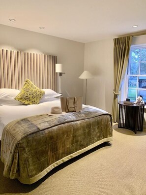 A hotel room with a bed, a bedside table, a lamp, a window with curtains, and a view of the outdoors. - Bedford Lodge Hotel and Spa (Newmarket)