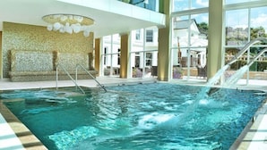 Ein großes Hallenbad mit Wasserfall, umgeben von großen Fenstern und einer Wand mit Musterung.