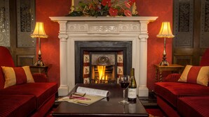 Une pièce avec une cheminée, des canapés rouges, une table avec une bouteille de vin et des verres, et des lampes décoratives.