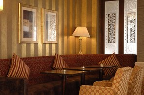 Ein Zimmer mit gestreifter Wand, einem Sofa mit gestreuten Kissen, einem Tisch mit Lampe und einem gemusterten Stuhl.