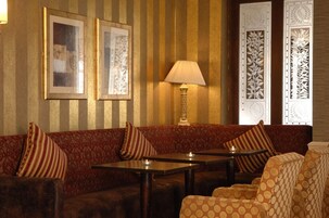 Una habitación con pared a rayas, un sofá con cojines a rayas, una mesa con lámpara y una silla estampada.
