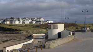 Une promenade en bord de mer bordée d’une rangée de maisons blanches, d’un petit bâtiment blanc et d’un chemin pavé agrémenté de bancs.