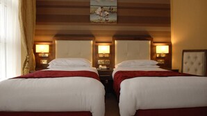 Een hotelkamer met twee bedden, elk met een rode deken, een schilderij erboven en bedlampjes.