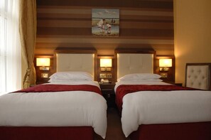 Een hotelkamer met twee bedden, elk met een rode deken, een schilderij erboven en bedlampjes.