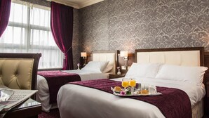 Een hotelkamer met twee bedden, een zithoek met een stoel, een klein tafeltje en een dienblad met ontbijtartikelen.