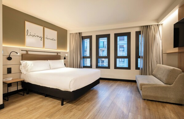 Une chambre d’hôtel avec un grand lit, une table de chevet, un téléviseur à écran plat et un canapé.