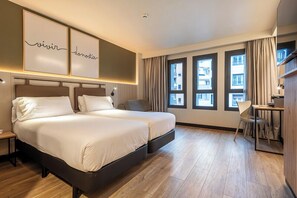Een hotelkamer met een groot bed, een bureau en uitzicht op de stad door grote ramen.