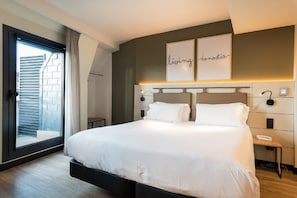 Una camera d'albergo moderna con un letto grande, una porta scorrevole in vetro per un balcone, un comodino con una lampada e un'opera d'arte a parete con le parole 'living' e 'domotix'.