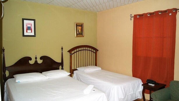 Una habitación con dos camas individuales, cabecero de madera, cortina roja y una mesita con un teléfono.
