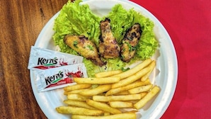 Un plato con alitas de pollo fritas, papas fritas y lechuga sobre una mesa de madera con una servilleta roja.