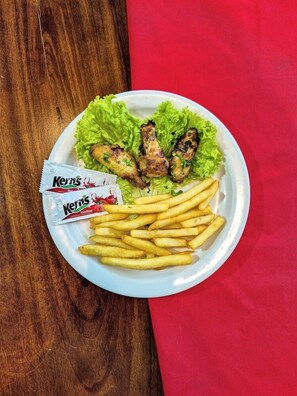 Ein Teller mit gebratenen Chicken Wings, Pommes und Salat auf einem Holztisch mit einer roten Serviette.