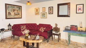 Un salón con un sofá rojo, una mesa de centro, una mesita auxiliar y una pared con cuadros enmarcados y un espejo.