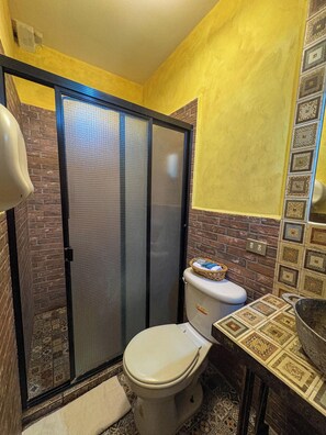 A bathroom with a shower enclosure, a toilet, and a sink with a patterned backsplash. - Hotel Rancho Argueta (San Luis Talpa)