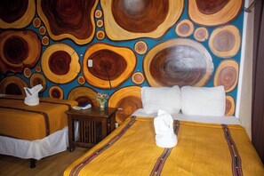 Quarto de hotel com duas camas, uma cabeceira de madeira, uma mesinha de cabeceira e uma parede com padrão circular.